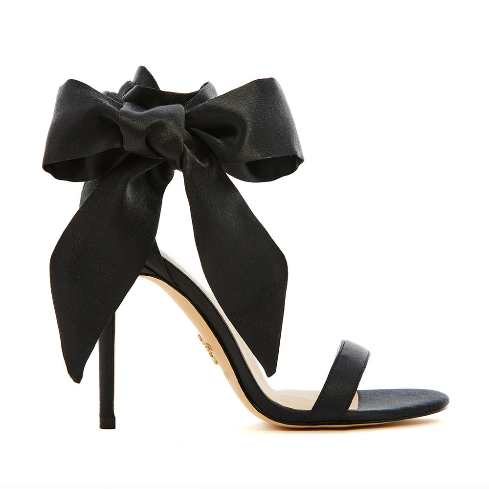 Elegant black high-heeled vegan sandal, featuring a statement vegan silk-satin bow, sleek ankle strap, and minimalist open-toe design, perfect for sophisticated and stylish occasions.