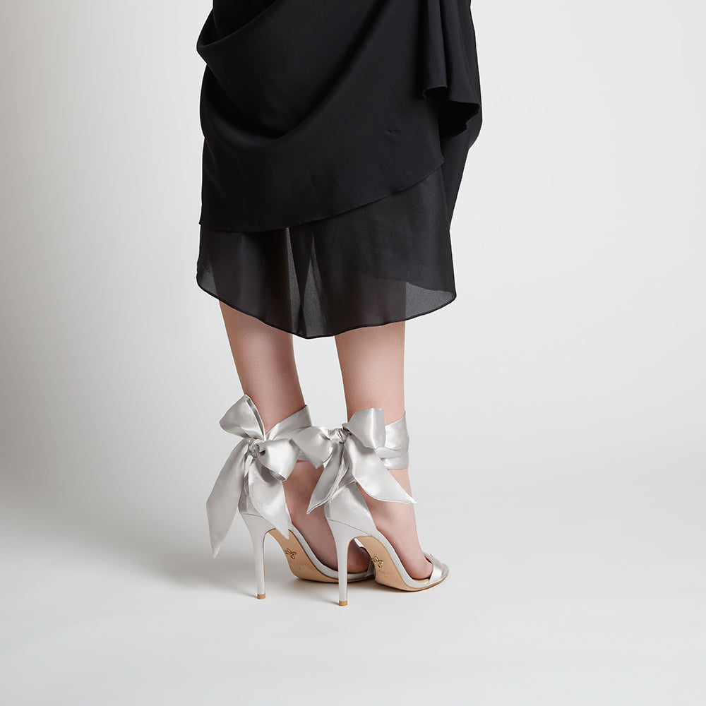 Elegant black high-heeled vegan sandal, featuring a statement vegan silk-satin bow, sleek ankle strap, and minimalist open-toe design, perfect for sophisticated and stylish occasions.
